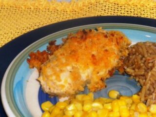A plate featuring a Kraft FreshTake crispy baked Cheesy Chicken breast, a serving of corn, and a portion of rice. The dish rests on a blue and green-rimmed plate atop a yellow textured placemat, enhancing its Southwestern flair.