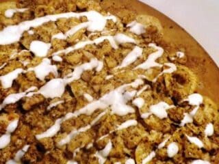 Pizza topped with flavorful jerk chicken pieces and drizzled with white sauce on a baking tray.