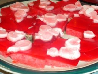 A plate with red Jello Treats, formed into squares and topped with small pink and white marshmallows. This delightful treat, reminiscent of a Be Still My Heart dessert, features gelatin and marshmallows arranged in a scattered pattern.