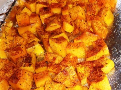 A baking tray lined with foil cradles cubed butternut squash, seasoned with spices. The low-calorie pieces are evenly roasted to a golden brown, boasting a slightly caramelized appearance that tempts the senses.