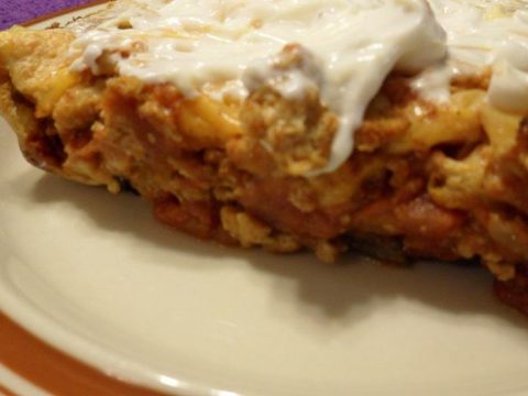 Close-up of a slice of Skinny Taco Pie casserole with a creamy, white topping on a plate with a brownish rim. The dish appears to contain beans and a mix of other ingredients, offering a hearty texture and appearance.