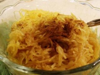 A glass bowl brimming with a delightful spaghetti squash recipe, crowned with a sprinkle of cinnamon. A fork rests invitingly at the side, ready to indulge.