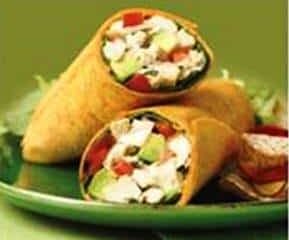 Two tortilla wraps brimming with chicken, avocado, and vibrant vegetables sit invitingly on a green plate against a matching background.