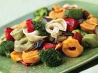 A vibrant tortellini vegetable salad features broccoli, red bell peppers, and eggplant pieces, all served on a light green square plate—a perfect lunchbox recipe bursting with color.