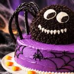 Spider cake, fun recipe: close-up of a chocolate spider with frosting fangs and licorice legs on a purple Halloween cake