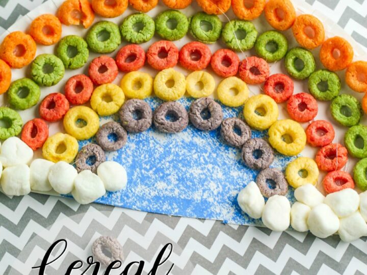 Colorful cereal rings are arranged in a rainbow pattern on zigzag paper, crafting a vibrant metaphor for finding joy at the end of the rainbow. Cotton balls at each end enhance this delightful scene. The text reads Cereal Rainbow Craft in a playful font.