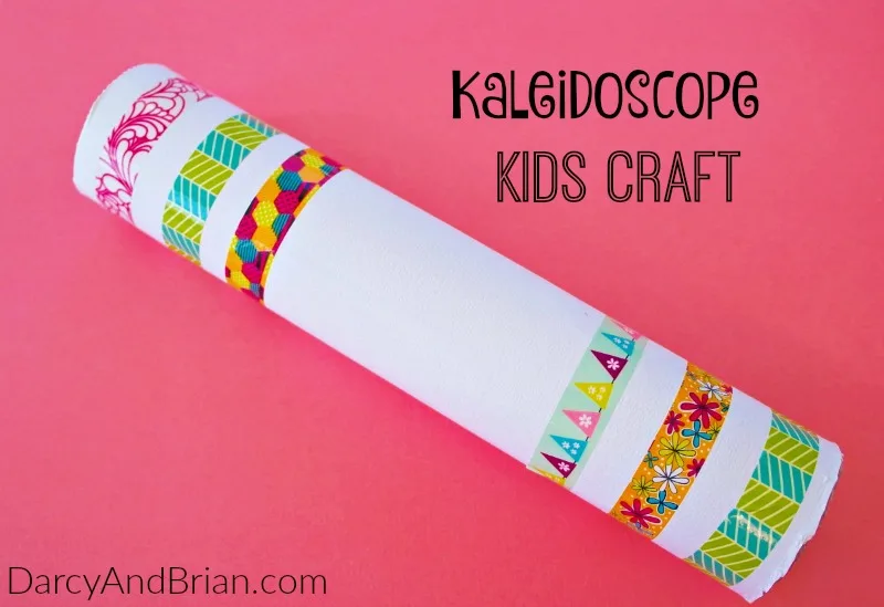 A homemade kaleidoscope craft, adorned with vibrant floral, chevron, and geometric tape designs, pops against a bright pink background. Text reads Kaleidoscope Kids Craft and DarcyAndBrian.com. Celebrate National Craft Month with endless crafty ideas!.