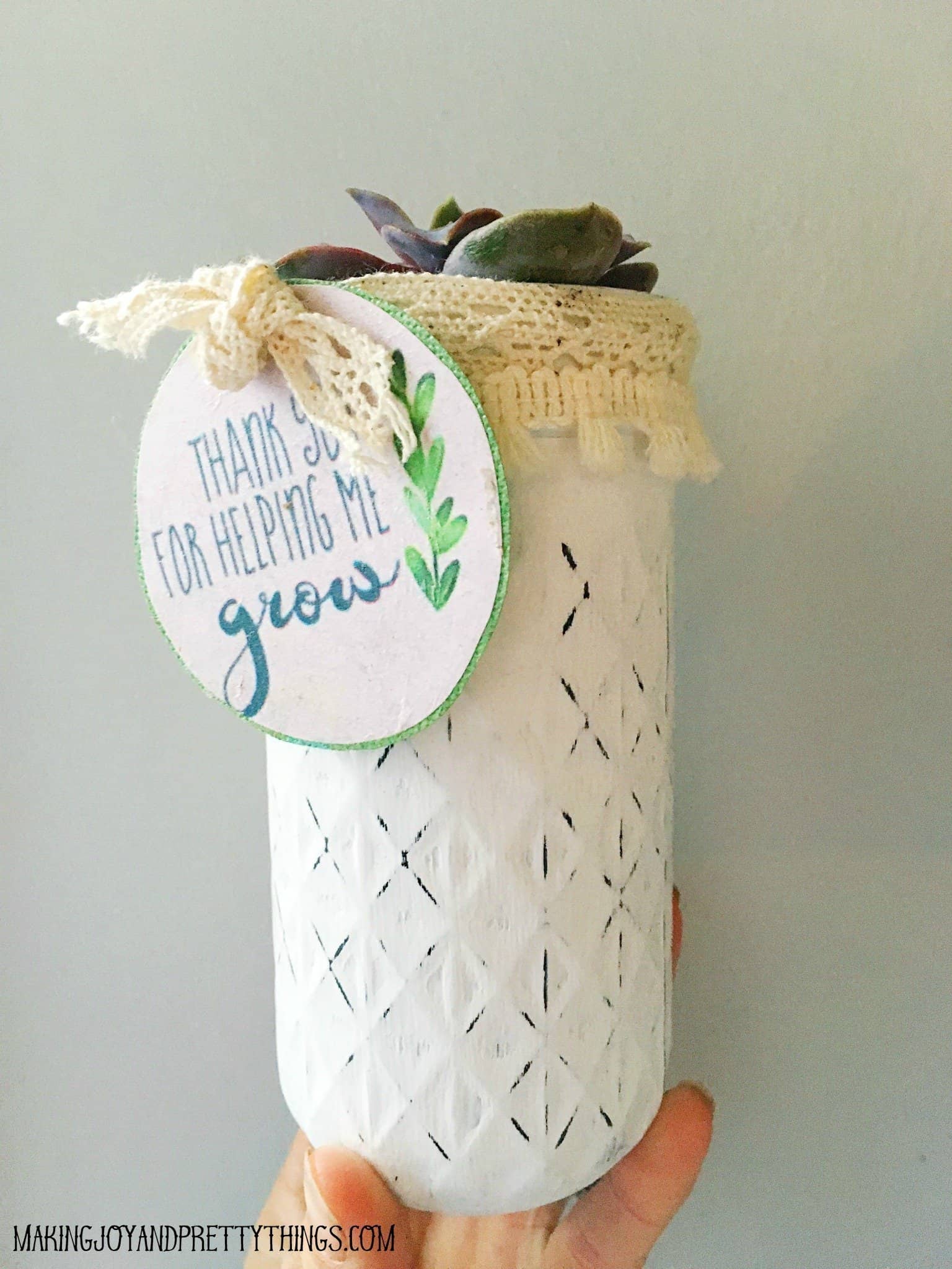 Decorative white mason jar with a lace lid holding a small succulent, featuring a tag that reads “Thank you for helping me grow.”