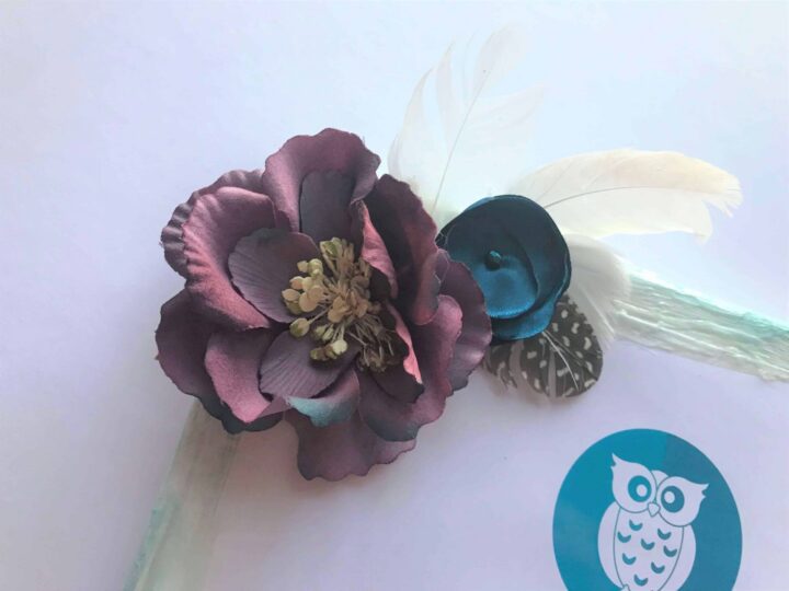 Close-up of a handmade paper flower embellishment with feathers and a button, used as decoration on a DIY teacher gift canvas.