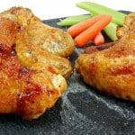 Grilled Chipotle Chicken Wings rest enticingly on a black slate board, accompanied by crisp celery sticks and vibrant baby carrots. A small white dish peeks from the background.
