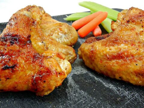 Grilled Chipotle Chicken Wings rest enticingly on a black slate board, accompanied by crisp celery sticks and vibrant baby carrots. A small white dish peeks from the background.