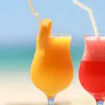 image of two tropical drinks with umbrellas on a fence surrounding a beach.