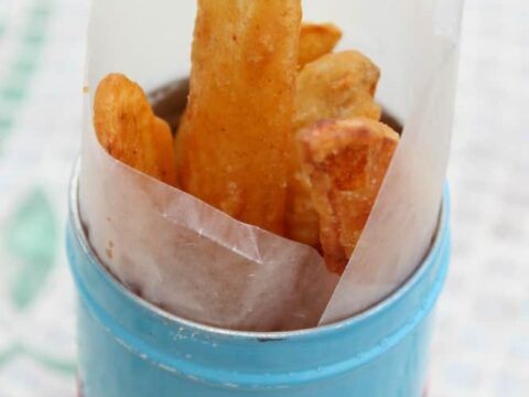 A small blue container with a red polka dot ribbon cradles homemade French fries snugly in parchment paper. Text at the top proudly declares, Homemade French Fries southernmomcooks.com. The backdrop offers a light checkered charm.