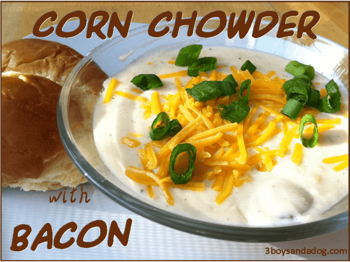A glass bowl of creamy corn chowder is topped with shredded cheddar cheese, crispy bacon, and chopped green onions. Two rolls sit beside the bowl, ready to savor. Text reads Corn Chowder with Bacon.