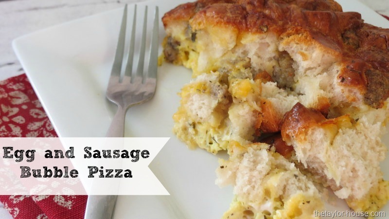 A slice of egg and sausage bubble pizza on a white plate with a fork, nestled on a red patterned napkin. Perfect for breakfast recipes for Christmas morning. Text on the image reads Egg and Sausage Bubble Pizza.