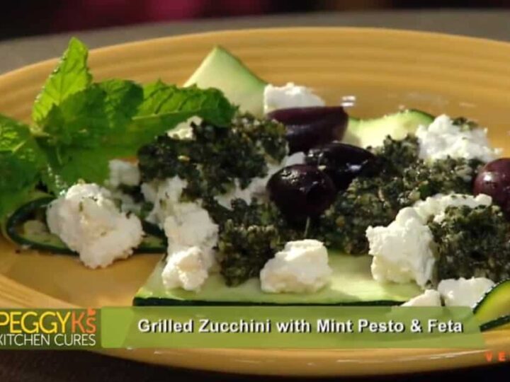 Discover the tantalizing Grilled Zucchini with Mint Pesto & Feta recipe, featuring perfectly grilled zucchini crowned with mint pesto, creamy feta cheese, and savory black olives. Fresh mint leaves add a final touch. Text on screen reads Peggy Ks Kitchen Cures.