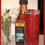 A bottle of Pure Leaf Lemon Iced Tea sits beside a glass of vibrant Watermelon Refresher Tea adorned with mint. White flowers in a glass jar create a serene backdrop, while Watermelon Refresher Tea is elegantly displayed at the top.