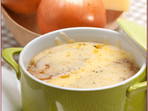 A green bowl of French Onion Soup, adorned with melted cheese, rests on a white saucer with a spoon. Background details include whole onions and a wedge of cheese. French Onion Soup is prominently displayed at the top, accompanied by a website URL below.