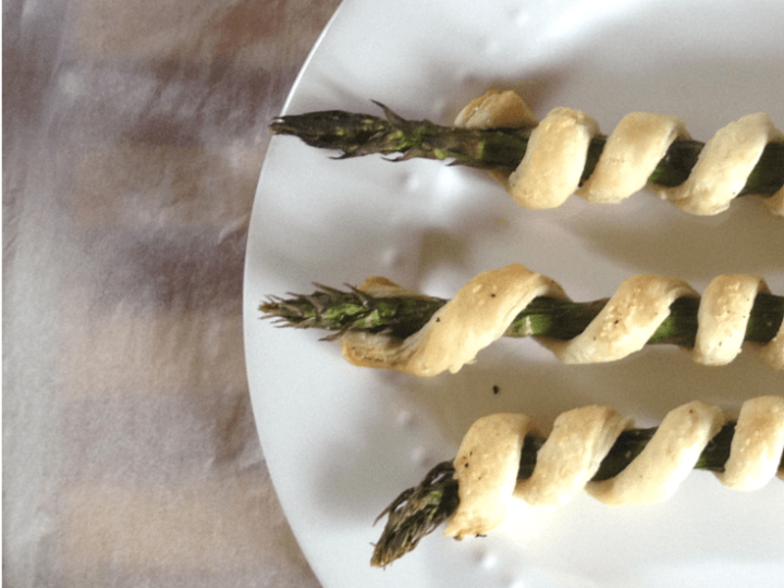 Three delectable Asparagus Spirals wrapped in golden pastry on a white plate. Text reads ASPARAGUS Spirals and In the Kids Kitchen in the corners, making it a delightful treat for little chefs.