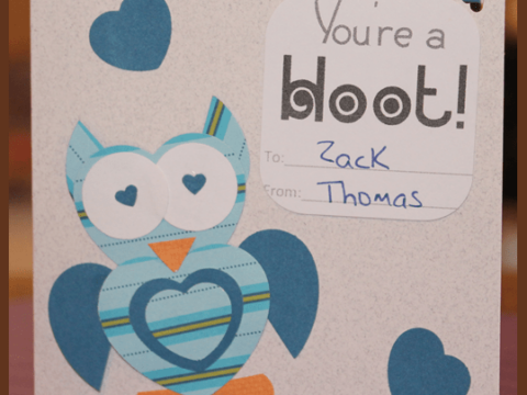 A handmade Heart Owl Valentine Card featuring punch art with blue and orange patterned papers. It reads Youre a hoot! with To: Zack From: Thomas penned inside. Blue heart shapes encircle the charming owl, adding an extra touch of affection.