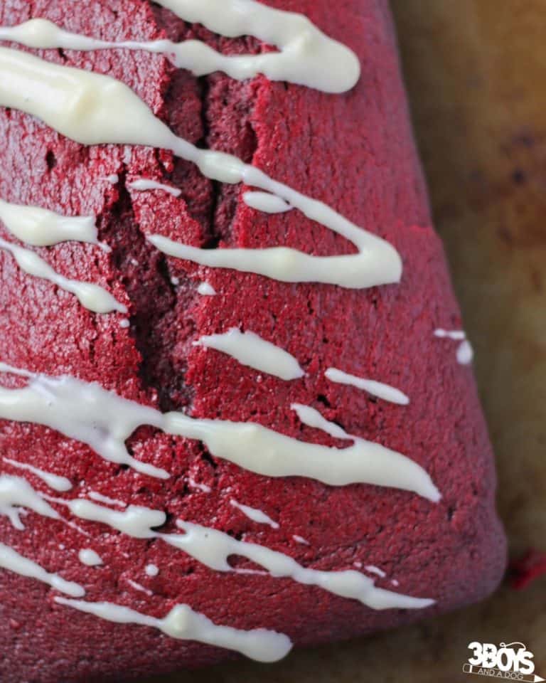 A red velvet biscotti drizzled with white chocolate icing rests on a baking sheet, embodying the rich flavors of a treasured red velvet bread recipe.