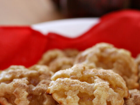 A white bowl filled with apple pie cookies, showcasing a lattice crust, sits on a red cloth. In the background, two apples add charm, evoking thoughts of Vermont crafts for kids. Text on the image reads APPLE PIE COOKIES www.SeeVanessaCraft.com.