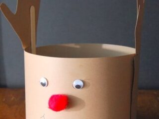A delightful paper reindeer hat complete with googly eyes, a red pom-pom nose, and hand-shaped antlers, perfect for those Arkansas crafts for kids projects. Its artfully placed on a wooden surface.