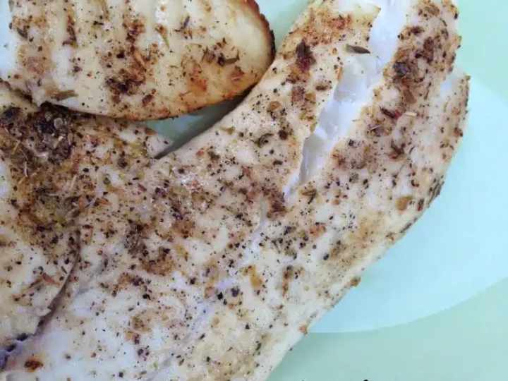 Grilled tilapia fillets seasoned with herbs and spices on a light green plate. The text reads Healthy Tilapia Recipes: Grilled Tilapia & Asparagus - A Seasonal Delight.