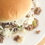 A close-up of a Philly Cheesesteak Sloppy Joe on a white plate. The sandwich is overflowing with seasoned ground beef, chopped green peppers, and melted cheese. Text overlays say Philly Cheesesteak Sloppy Joes and Easy Dinner.