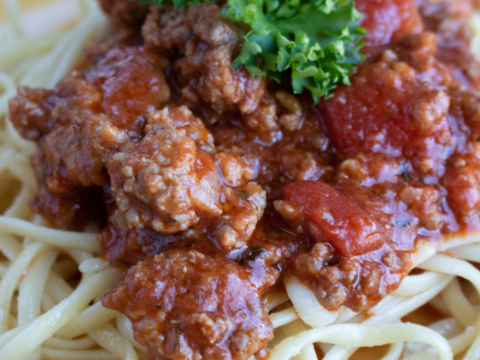 A plate of Instant Pot spaghetti topped with a hearty meat sauce and garnished with fresh parsley, served on a yellow dish.