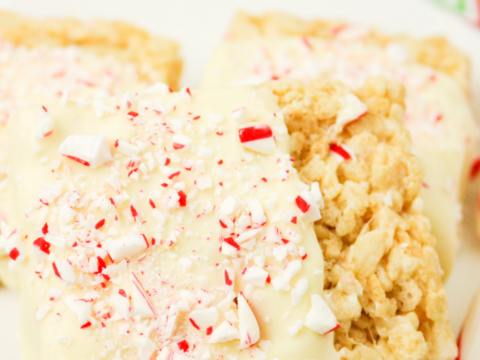 A close-up of three White Chocolate Peppermint Rice Krispies treats on a white plate. Each delight is topped with crushed peppermint candies and rests on a red and green chevron-patterned napkin.