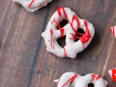 A delightful spread of white chocolate-covered pretzels drizzled with red icing sits on a wooden surface, mingling with red and white striped candy canes—a perfect setting for a festive peppermint pretzels recipe.