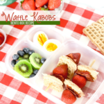The Bento Waffle Kabobs feature delectable waffle pieces, juicy strawberries, and crispy bacon on skewers. Sides of kiwi slices, blueberries, and a boiled egg half complete the meal, all elegantly presented on a red and white checkered cloth.