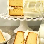 slice of cake on a white plate with cake on cake stand behind