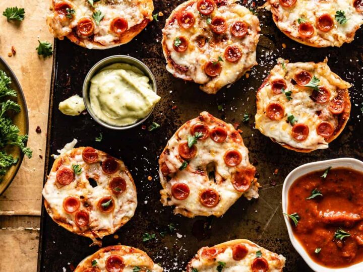 Mini bagel pizzas topped with melted cheese and pepperoni, served on a baking tray with dipping sauces.