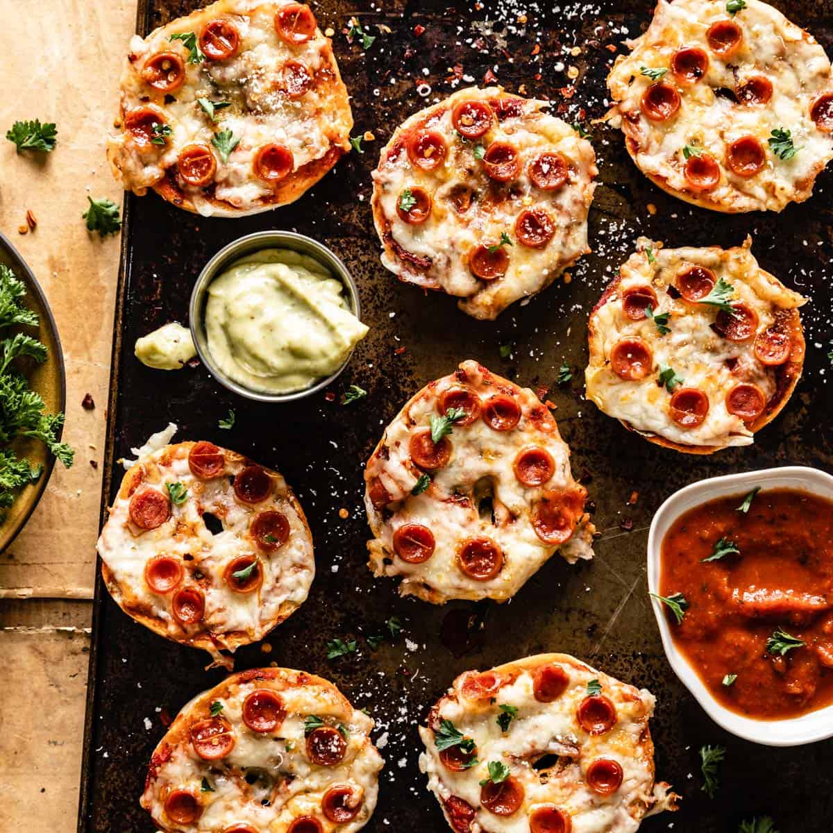 Mini bagel pizzas topped with melted cheese and pepperoni, served on a baking tray with dipping sauces.