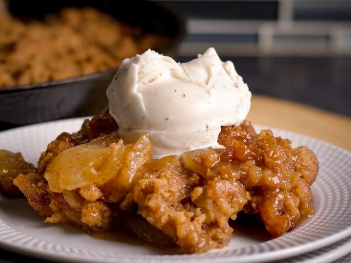 Serving of apple crisp with cinnamon apples and crumb topping, topped with a scoop of vanilla ice cream on a plate.