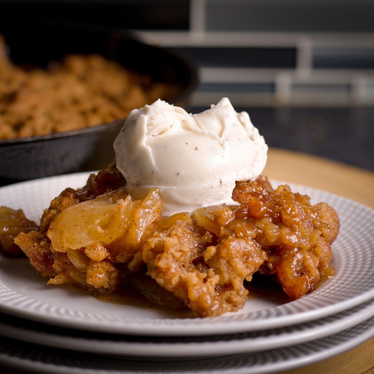Serving of apple crisp with cinnamon apples and crumb topping, topped with a scoop of vanilla ice cream on a plate.