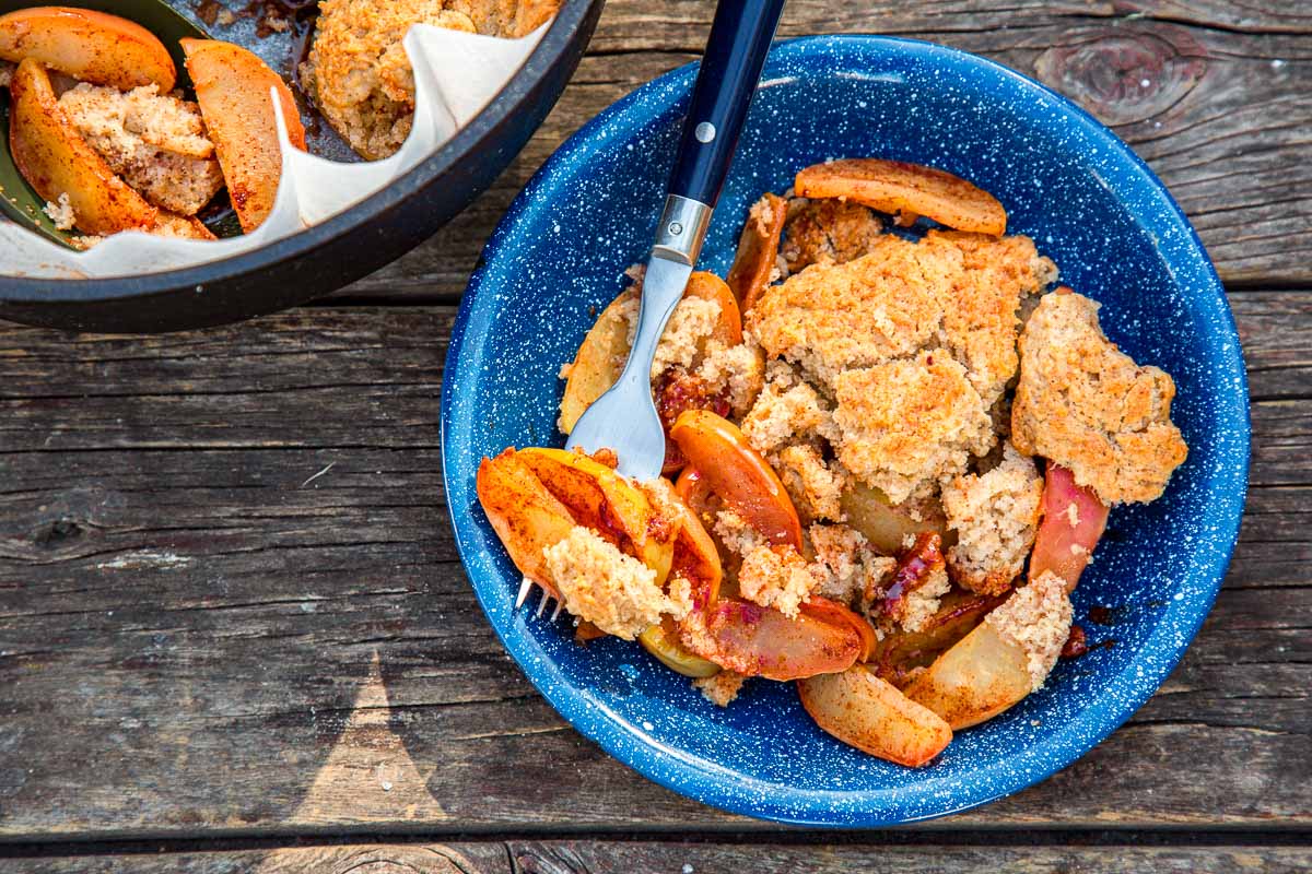 Blue bowl filled with warm apple crisp topped with crumbly streusel and sliced baked apples, served with a fork on a rustic wooden table.