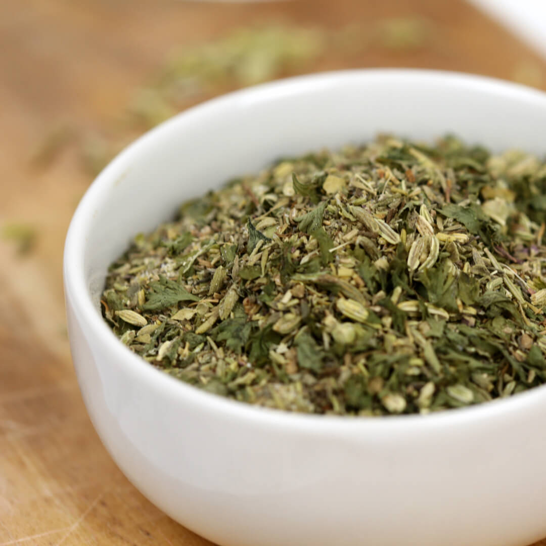 Small white bowl filled with a homemade dried herb seasoning blend on a wooden surface.
