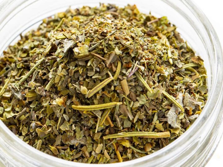 Glass jar filled with Italian seasoning blend made of dried herbs like oregano, basil, and rosemary.