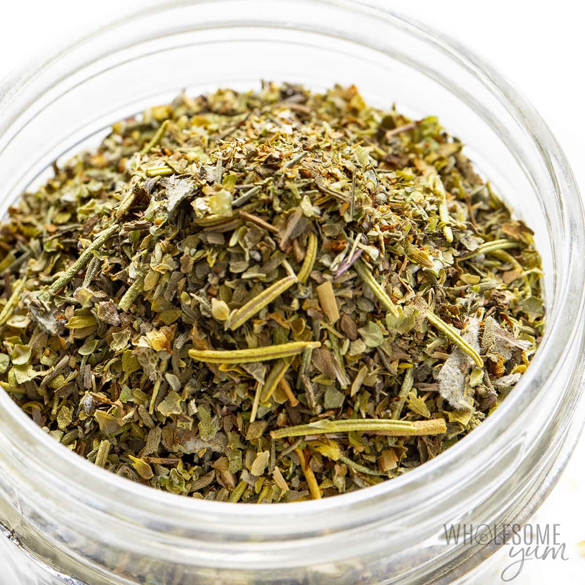 Glass jar filled with Italian seasoning blend made of dried herbs like oregano, basil, and rosemary.