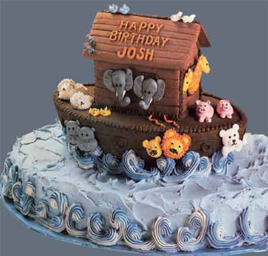 A birthday cake shaped like Noahs Ark, with animal figures like elephants, lions, and pigs on the ark. The cake is decorated with blue icing waves and has the message Happy Birthday Josh on top.
