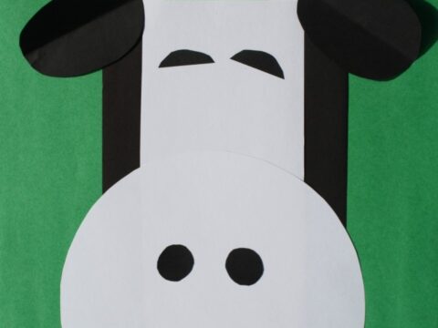 A craft made from paper in the shape of a cows face, using geometric shapes like circles and ovals. The background is green, and the text reads Easy Cow Shapes Craft.