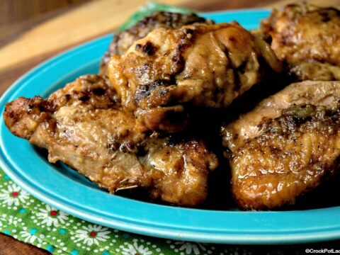 A blue plate filled with juicy, cooked chicken pieces, placed on a floral-patterned green cloth. The chicken has a crispy, browned exterior.