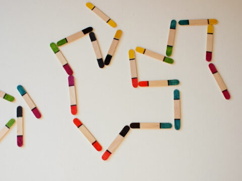 Colorful craft sticks arranged on a white surface in the shape of a heart and an arrow.