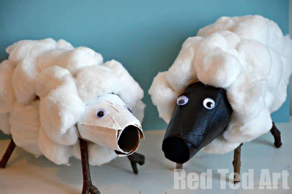 Two sheep crafts made from recycled materials. The sheep bodies are covered in white cotton balls, with faces made from painted cardboard tubes and googly eyes. They stand on twig legs against a blue background. Red Ted Art text is in the corner.