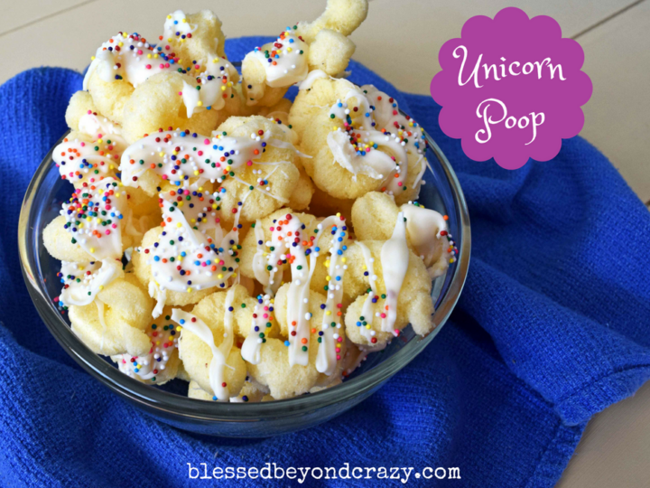 A bowl of puffed corn drizzled with white chocolate and colorful sprinkles, placed on a blue cloth. A purple label reads Unicorn Poop. The website blessedbeyondcrazy.com is visible at the bottom.