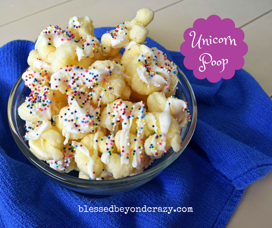 A bowl of puffed corn drizzled with white chocolate and colorful sprinkles, placed on a blue cloth. A purple label reads Unicorn Poop. The website blessedbeyondcrazy.com is visible at the bottom.