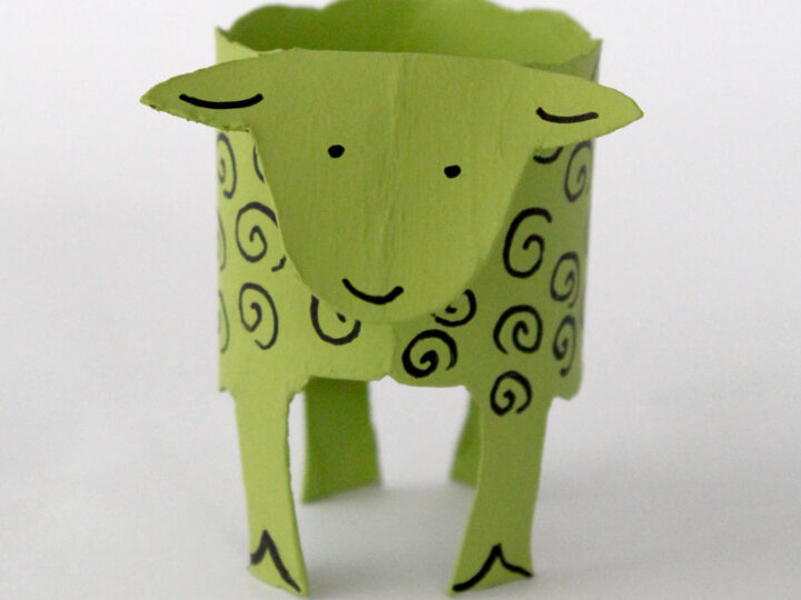 A green paper sheep craft made from a recycled cardboard roll. The sheep has a simple face with a smile and curly black lines representing wool. Text at the bottom right reads “The Craft Train.”.